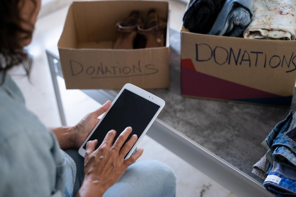 woman using a digital tablet while preparing a box of clothes for donation