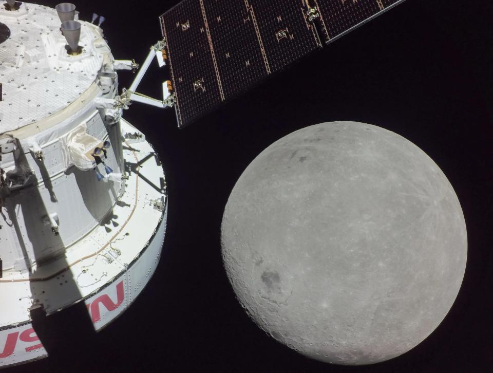 the back of a spacecraft is in view with the approaching moon.