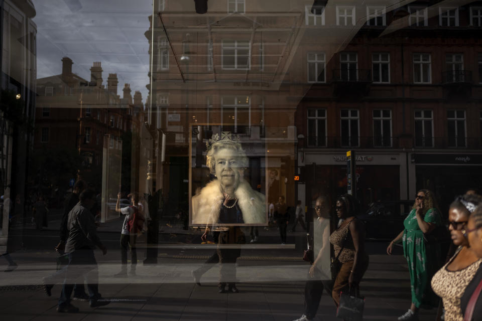 People walk past a portrait of Queen Elizabeth II photographed inside a shop in central London, Monday, Sept. 12, 2022. Queen Elizabeth II, Britain's longest-reigning monarch and a rock of stability across much of a turbulent century, died Thursday Sept. 8, 2022, after 70 years on the throne. She was 96. (AP Photo/Emilio Morenatti)