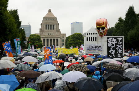 People hold placards as they take shelter against the rain during a mass rally against Japan's Prime Minister Shinzo Abe's security bill outside the parliament in Tokyo August 30, 2015. REUTERS/Thomas Peter