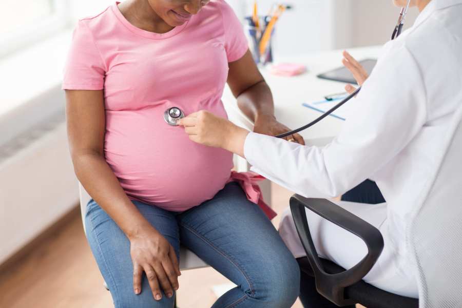 pregnancy, medicine, healthcare and people concept – close up of gynecologist doctor with stethoscope listening to pregnant african american woman baby heartbeat at hospital