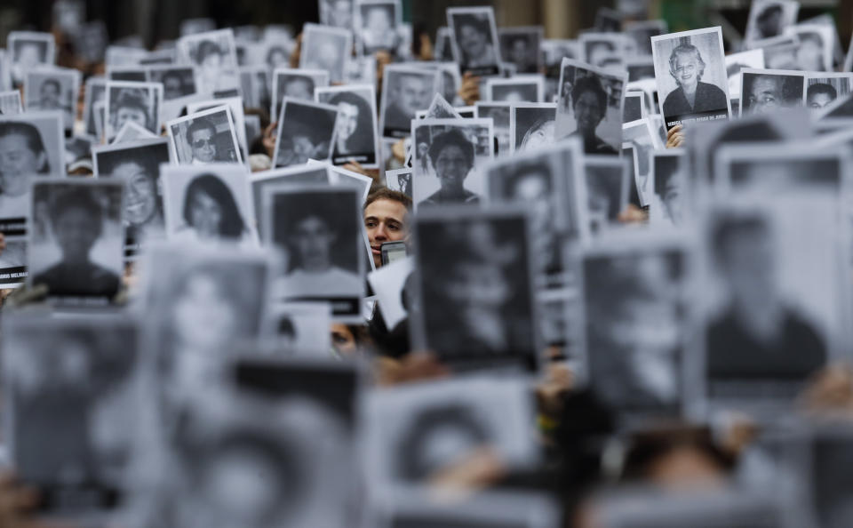 A man stands amid pictures of victims of the bombing of the AMIA Jewish center that killed 85 people, on the 25th anniversary of the attack in Buenos Aires, Argentina, Thursday, July 18, 2019. (AP Photo/Natacha Pisarenko)