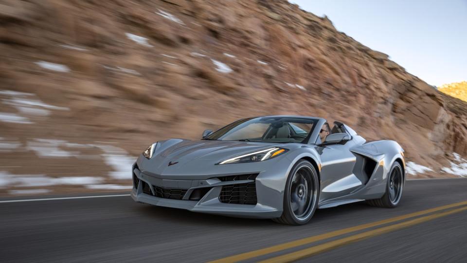 front 34 view of a 2024 corvette e ray 3lz convertible in sea wolf gray tricoat driving on a mountain road pre production model shown actual production model may vary model year 2024 corvette e ray available 2023