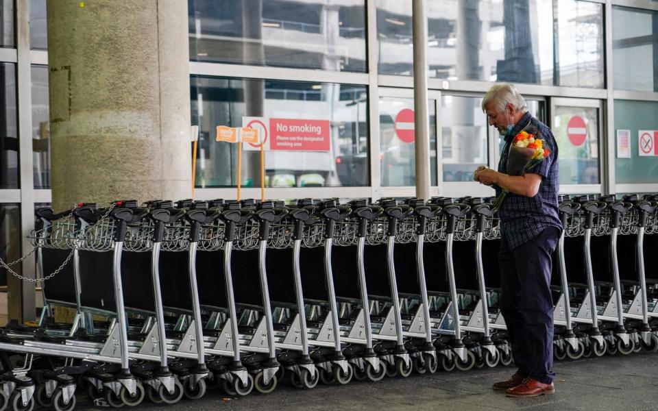 A man holds a bouquet of flowers at Gatwick Airport, London, as vaccinated travellers from US and parts of Europe are allowed to enter Britain - AP/Alberto Pezzali