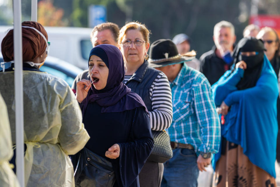 A woman places a Covid-19 testing swab in her mouth as others line up behind her at a pop-up testing site. Source: Getty