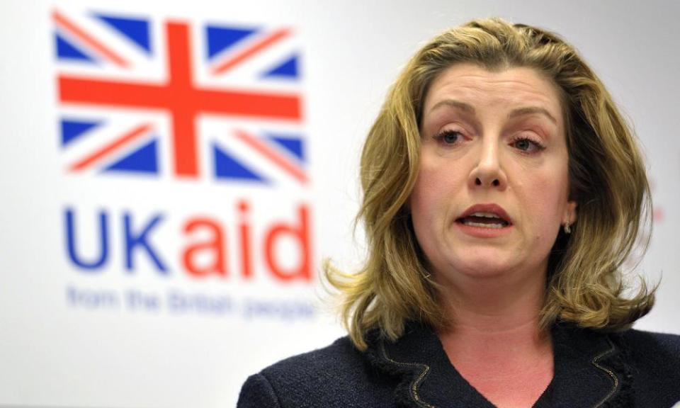 International Development Secretary Penny Mordaunt stands in front of a UK Aid sign.