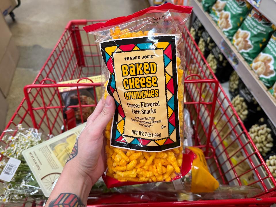 hand holding up a bag of baked cheese crunchies over a cart at trade joes