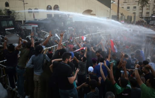 Iraqis waving national flags are being sprayed with water cannon by security forces during a demonstration in the capital Baghdad on July 20, 2018