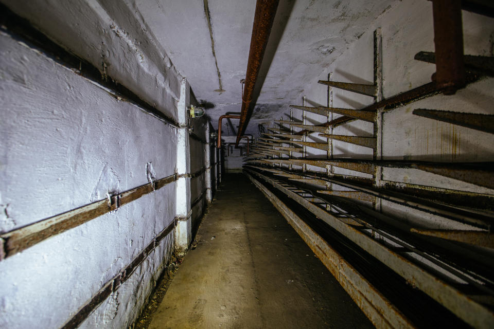 Long, narrow corridor of an old, abandoned building with rusting metal pipes and decaying walls