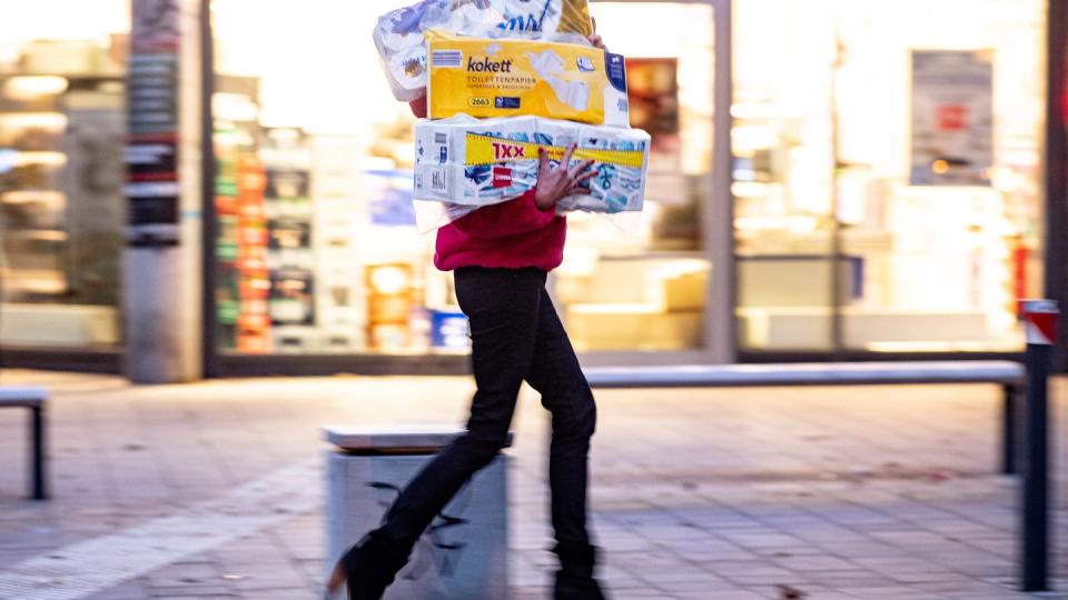 Ein Frau läuft mit dem Arm voller Klopapierrollen aus einem Drogeriemarkt heraus.