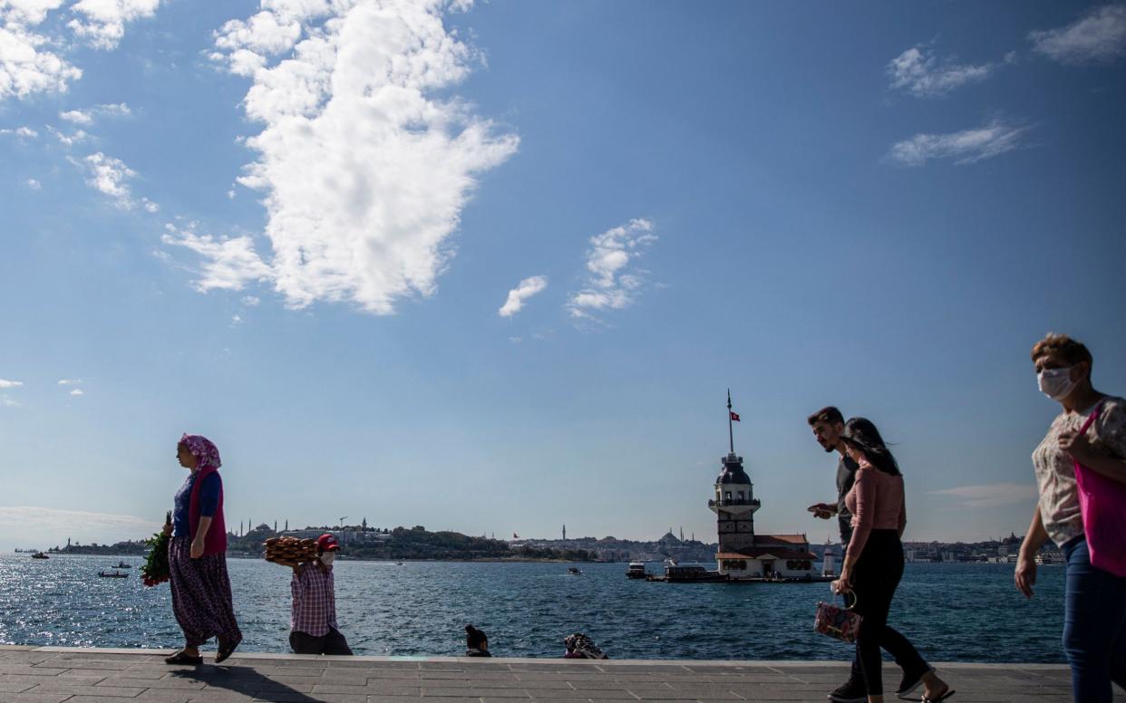 People spend time near the Bosphorus by the Maiden's tower and the Hagia Sophia Grand Mosque in Istanbul, Turkey - Shutterstock