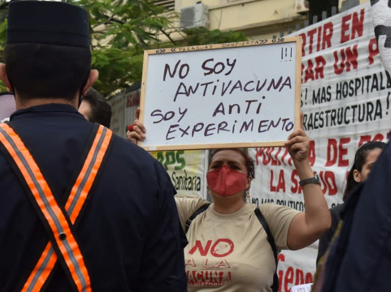 Une femme brandit une pancarte sur lequel est écrit "Je ne suis pas anti-vaccin, je suis anti-expérience" lors d'une manifestation contre la vaccination obligatoire devant le ministère de la Santé à Asuncion, au Paraguay le 11 janvier 2022 (AFP/Daniel Duarte)