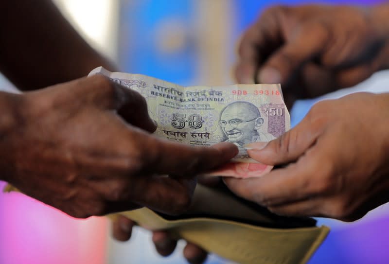 FILE PHOTO: A customer hands a 50-Indian rupee note to an attendant at a fuel station in Ahmedabad