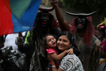 A child reacts next to members of a folk group dressed as devils while taking part in the celebration of Los Palmeros de Chacao, a Holy Week tradition, in Caracas, Venezuela, April 13, 2019. REUTERS/Ivan Alvarado