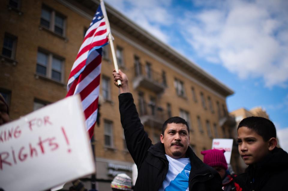 Immigrant man wearing a Guatemalan flag shirtholds an American flag.