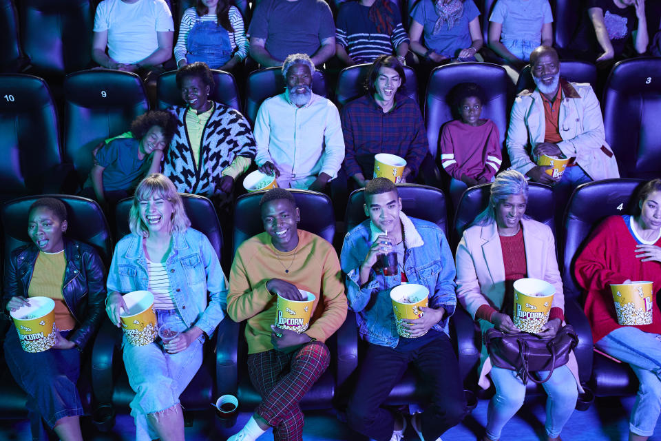 Multi-ethnic audience enjoying popcorn while watching comedy movie at cinema hall