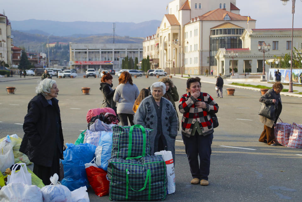 Ethnic Armenians refugees stand with their bags and wait for their relatives as they return to Stepanakert, the capital of the separatist region of Nagorno-Karabakh, on Tuesday, Nov. 17, 2020. Russian peacekeepers have started to move into the region, a total of 1,960 of them are to be sent in under a five-year mandate. Russia's Defense Ministry reported that the peacekeepers accompanied about 1,200 people returning to Nagorno-Karabakh from Armenia since Saturday. (AP Photo/Sergei Grits)