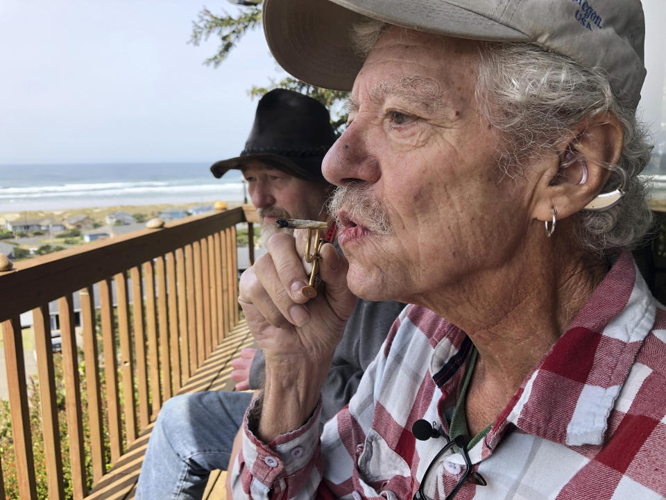 In this April 25, 2019, photo, two-time cancer survivor and medical marijuana cardholder Bill Blazina, 73, smokes a marijuana joint on the deck of his neighbor's home in Waldport, Ore. Blazina also uses a high-potency marijuana oil as a medical marijuana patient but he can't afford it at a recreational marijuana store. Blazina has learned how to make his own oil in a rice cooker after watching online videos. (AP Photo/Gillian Flaccus)