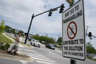 Adam Atnip, who is homeless and lives in his car, panhandles near a sign asking people not to give directly to panhandlers on May 10, 2022, in Cookeville, Tenn. Tennessee is about to become the first U.S. state to make it a felony to camp on local public property such as parks. (AP Photo/Mark Humphrey)