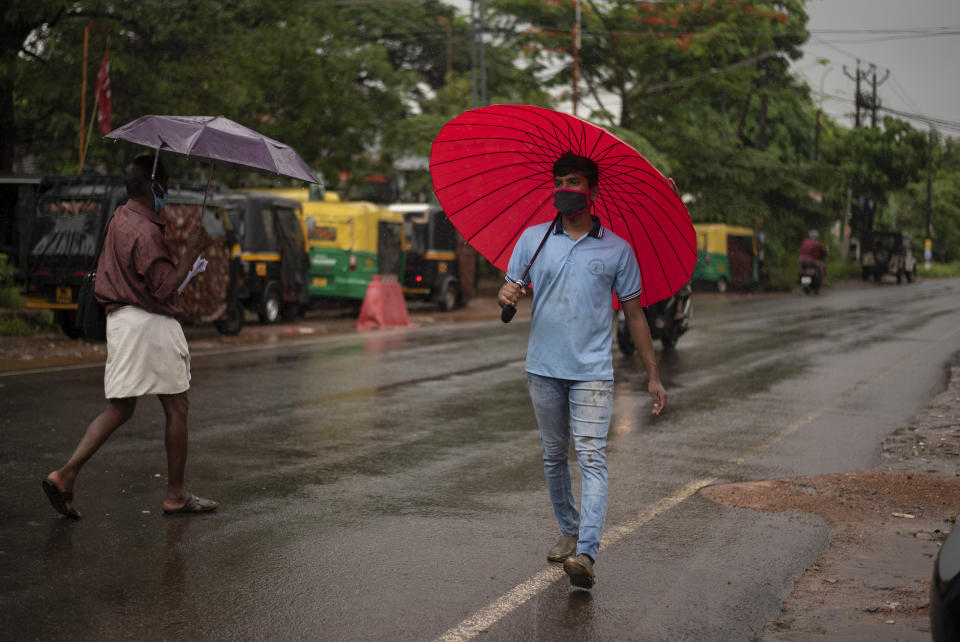 People wearing masks as precaution against the coronavirus walk holding umbrellas during monsoon rains in Kochi, Kerala state, India, Saturday, June 6, 2020. India which surpasses Italy as the sixth worst-hit by the coronavirus caseload is trying to contain the chain of transmission while allowing social and economic activity to resume. (AP Photo/ R S Iyer)