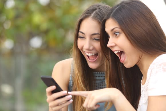 Two teen girls smiling while looking at a smartphone.