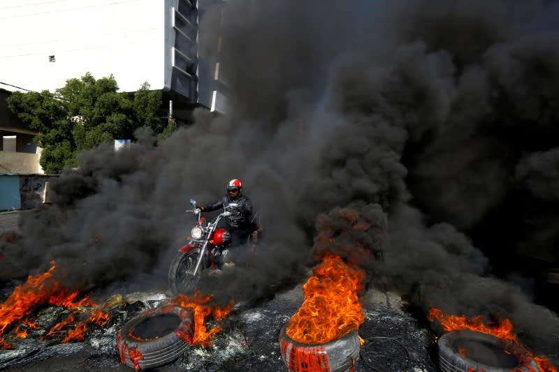 A man rides a motorcycle between burning tires during ongoing anti-government protests in Najaf