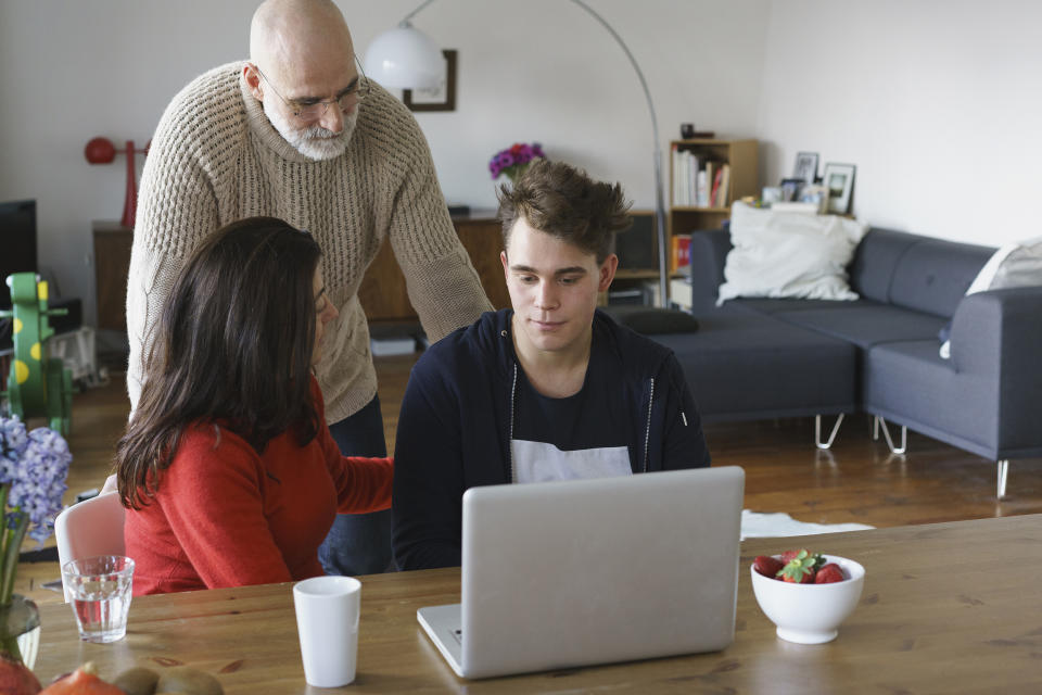 Parents talking with son by table with laptop at home (Getty Images stock)