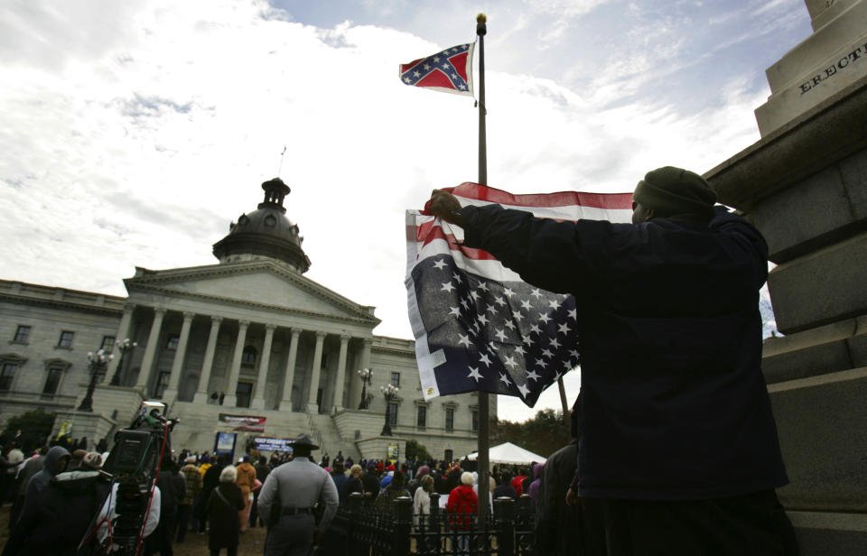 FILE - Dexter Suber of New York, holds an American flag upside down as he protests the Confederate flag that is on the Statehouse grounds during a rally for Martin Luther King Day at the Capitol in a Monday Jan. 16, 2012 file photo in Columbia, S.C. Iowa, South Carolina and South Dakota recently joined Nebraska in agreeing to share driver's license information with the U.S. Census Bureau to help the Trump administration with the controversial task of figuring out the citizenship status of every U.S. resident. (AP Photo/Mary Ann Chastain, File)