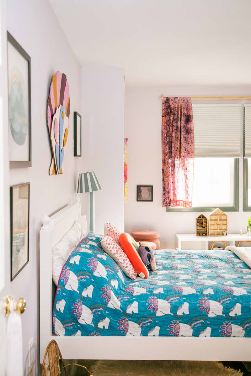 Blue coverlet on bed in white bedroom with short curtains on window.