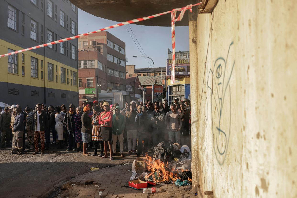 People standing at a bonfire look on as unseen firefighters work at the scene of a fire in a building in Johannesburg on 31 August. (AFP via Getty Images)