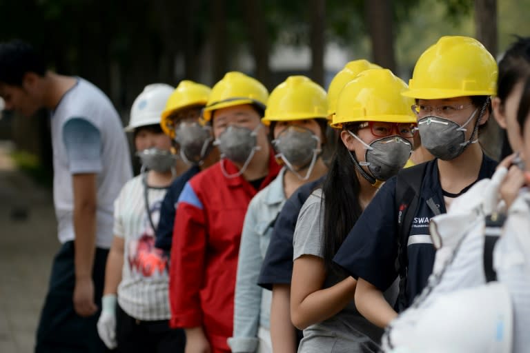 Chinese workers wearing face masks stand outside a factory in Tianjin on August 16, 2015