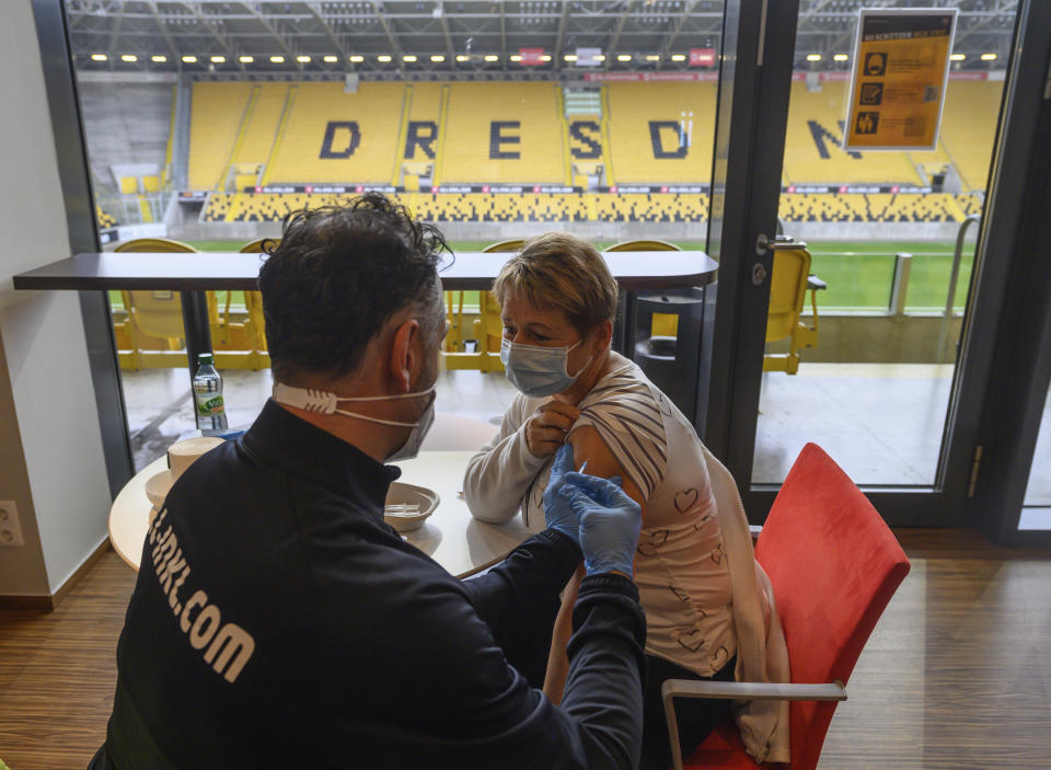 Onays Al-Sadi , left, team doctor of soccer club SG Dynamo Dresden, inoculates awoman with Moderna's vaccine against the coronavirus in a VIP lounge during a vaccination campaign at the Rudolf Harbig Stadium, the home ground of the second division football team in Dresden, Germany, Tuesday, Dec. 14, 2021.(Robert Michael/dpa via AP)