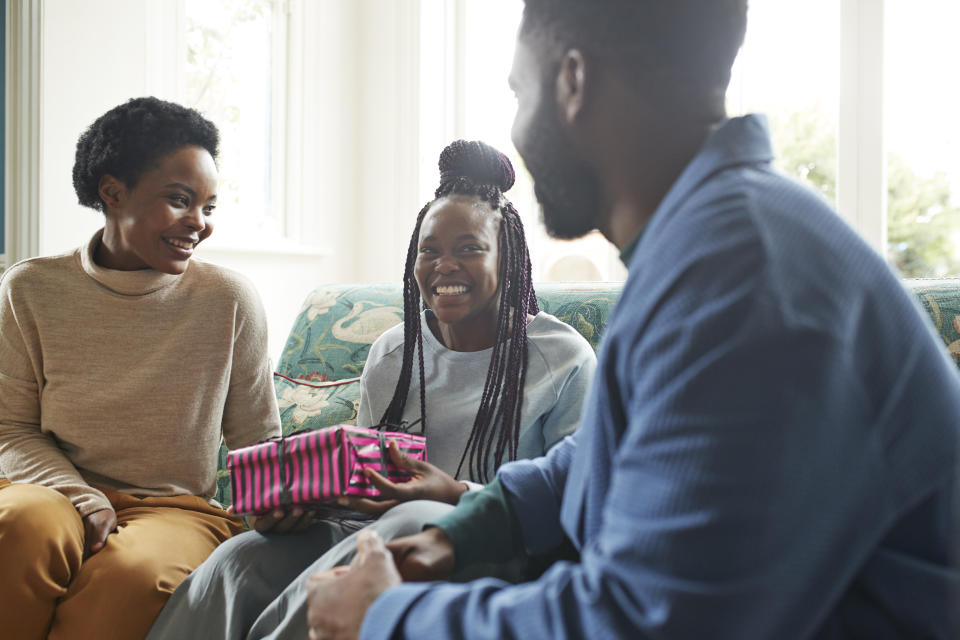 Cheerful teenage girl holding present while sitting with family on sofa at home during Christmas 