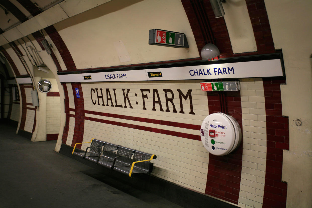 A station wall that reads 'chalk farm' in maroon coloured tiles. There's a bench and a help station 