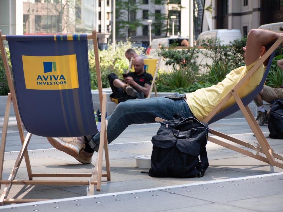 office workers sit in the sun on Aviva deckchairs outside the Aviva headquarters in London,
