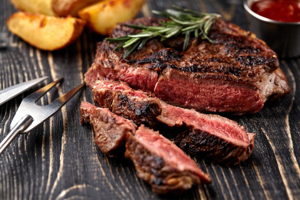 Juicy steak medium rare beef with spices on wooden board on table. dry aged. Served with potatoes and tomato sauce. Still life