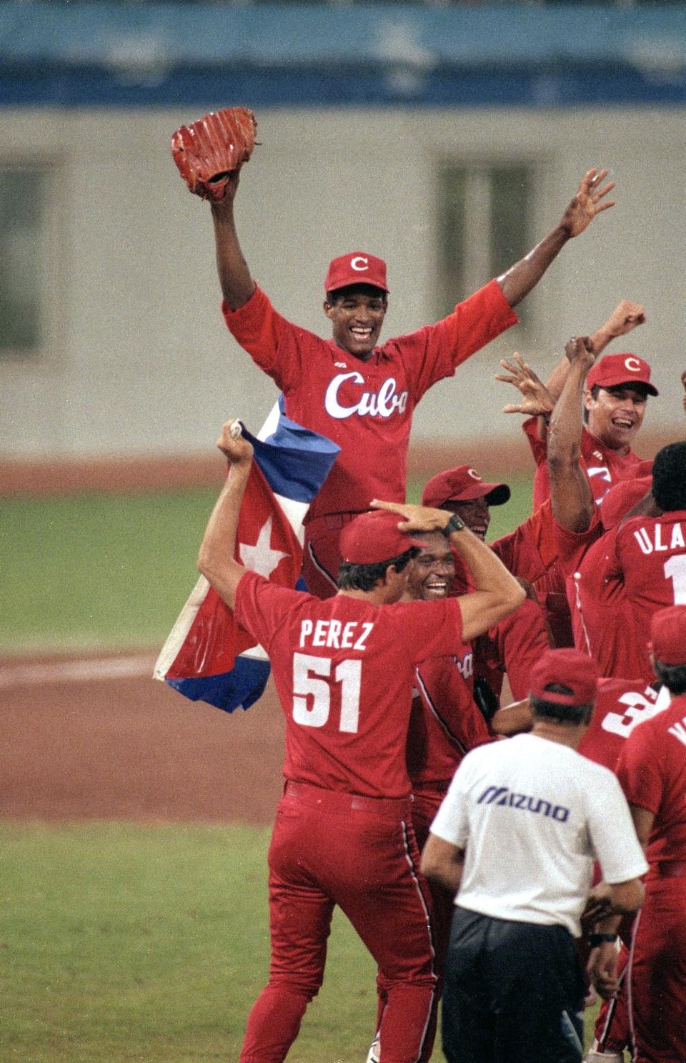 Members of the Cuban baseball team celebrating on the field, with one player, wearing jersey number 51 (Perez), proudly holding a Cuban flag