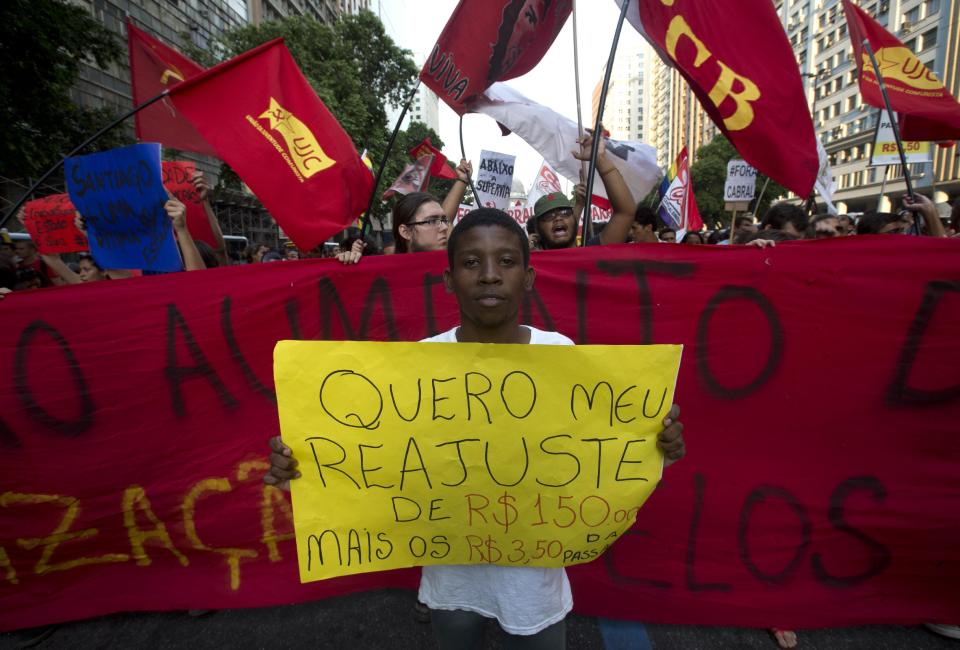 A young man holds a sign that reads in Portuguese; "I want a readjustment," in reference to the increased bus fare, protesting not only against a 10-cent hike in bus fares but demanding the government lower the price from the previous fare, in Rio de Janeiro, Brazil, Thursday, Feb. 13, 2014. Some roads in the center of Rio, which will serve as the 2016 Olympic city, were blocked Thursday night as demonstrators carried banners calling for a reversal of the fare hike, along with more investments in education and health care. (AP Photo/Silvia Izquierdo)