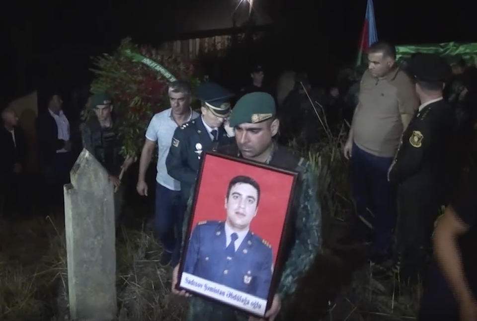 In this image taken from video, a serviceman carries a portrait of Azeri serviceman Shamistan Sadykhov killed at Azerbaijani-Armenian border, during his funeral in Lerik, Azerbaijan, Tuesday, Sept. 13, 2022. Armenia and Azerbaijan accused each other of new rounds of shelling on Wednesday morning as hostilities reignited between the two longtime adversaries. (AP Photo)