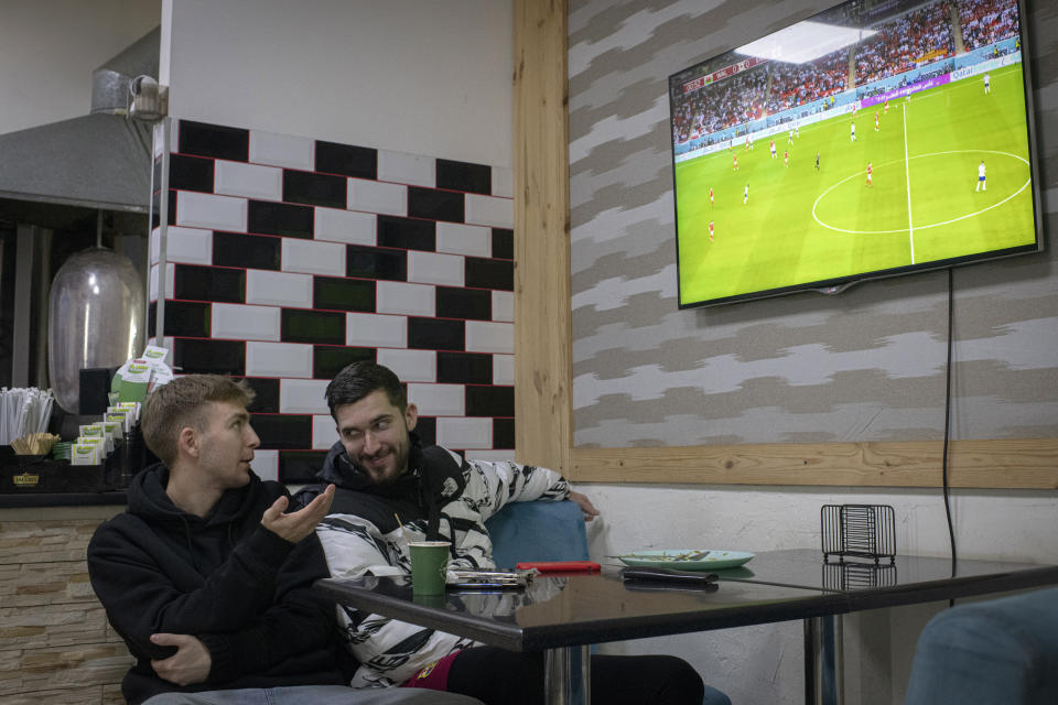 Hlib Kuian, left, and Roman Kryvyi watch a World Cup soccer match on a screen at Mazza Cafe kebab-stand, in Irpin, Kyiv region, Ukraine, Tuesday, Nov. 29, 2022. For soccer lovers in Ukraine, Russia's invasion and the devastation it has wrought have created uncertainties about both playing the sport and watching it. For Ukrainians these days, soccer trails well behind mere survival in the order of priorities. (AP Photo/Andrew Kravchenko)