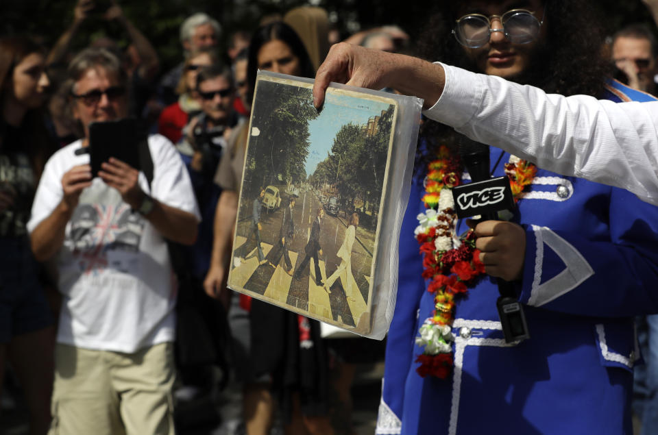 A fan carries a copy of the album 'Abbey Road' as he crosses the Abbey Road zebra crossing on the 50th anniversary of British pop musicians The Beatles doing it for their album cover of 'Abbey Road' in St Johns Wood in London, Thursday, Aug. 8, 2019. They aimed to cross 50 years to the minute since the 'Fab Four' were photographed for the album. (AP Photo/Kirsty Wigglesworth)