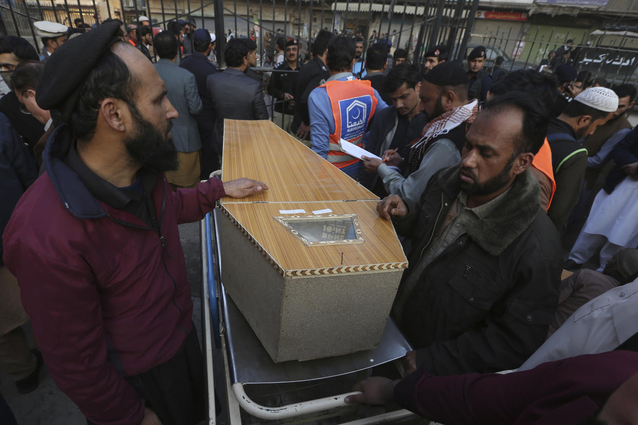 People wait for transport next to a coffin of their relative, killed in the suicide bombing inside a mosque, after collecting from a hospital, in Peshawar, Pakistan, Monday, Jan. 30, 2023. A suicide bomber struck Monday inside a mosque in the northwestern Pakistani city of Peshawar, killing multiple people and wounding scores of worshippers, officials said. (AP Photo/Muhammad Sajjad)