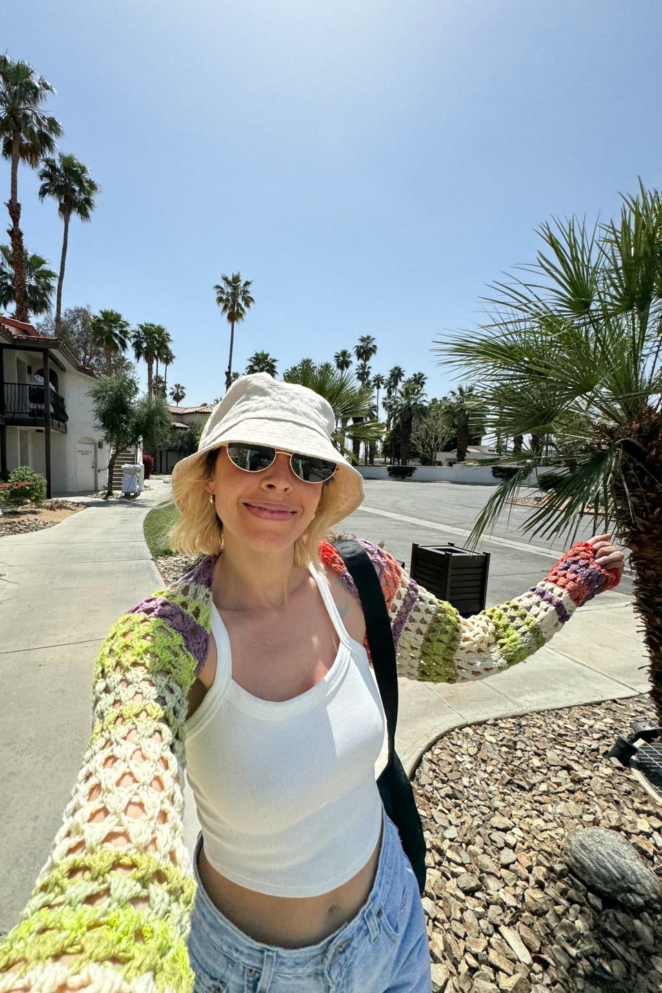 Woman in a sunhat and sunglasses takes a selfie on a sunny street with palm trees