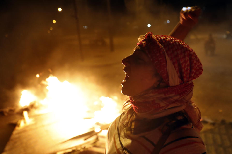 An anti-government protester chants slogans as others burn wood and barriers to block a road during a protest against the political leadership they blame for the economic and financial crisis, in Beirut, Lebanon, Thursday, June 11, 2020. (AP Photo / Hussein Malla)