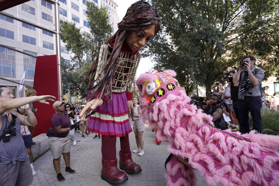 Little Amal, a 12-foot puppet of a 10-year-old Syrian refugee girl, center, is greeted by a performer in a lion dance costume, right, near the Chinatown neighborhood of Boston, Thursday, Sept. 7, 2023. Little Amal is scheduled to journey across the United States, with planned stops in over 35 towns and cities, between Sept. 7 and Nov. 5, 2023, in an effort to raise awareness about refugees and displaced people across the world. (AP Photo/Steven Senne)