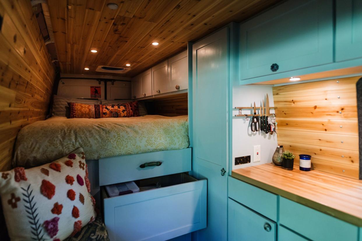 interior living space with bed on the left and light blue cupboards and kitchen on the right, of a van converted into a home