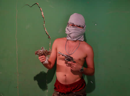 An MS-13 gang member poses for a photograph as he holds a gun and a bag of marijuana in San Pedro Sula, Honduras, October 6, 2018. REUTERS/Goran Tomasevic