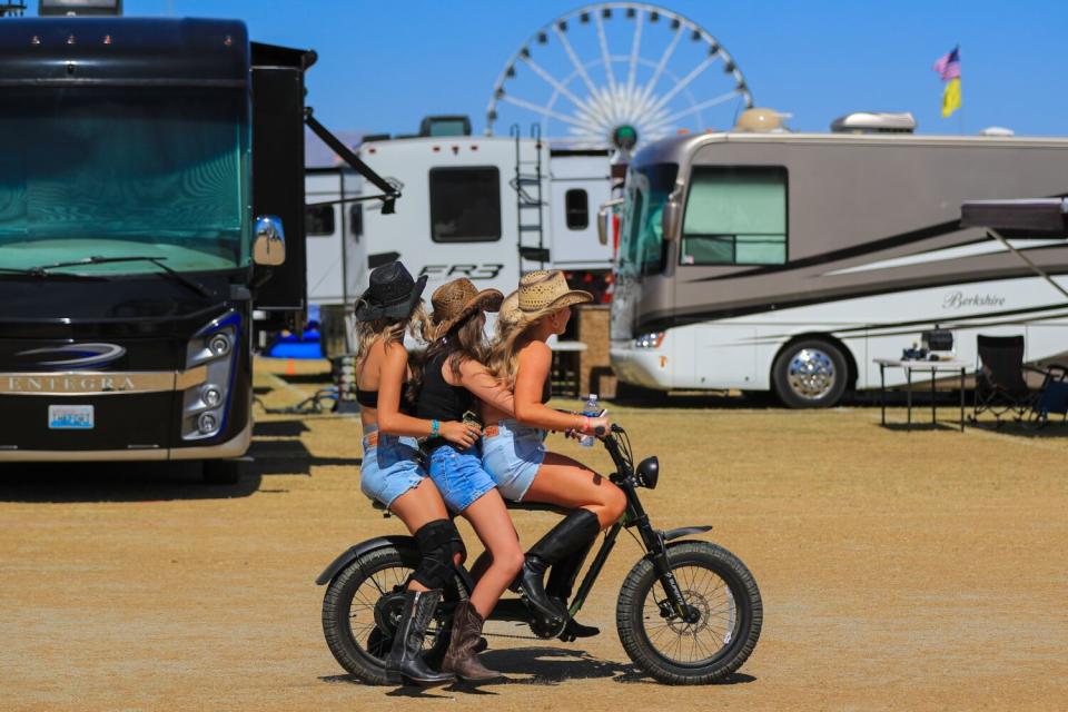 Three women in cowboy boots and hats and shorts ride an electric bike together on the Stagecoach campground.