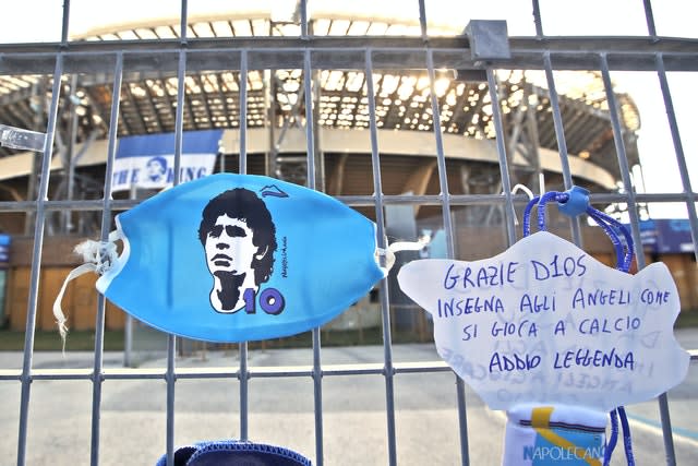 A sign which reads 'Thank you God, teach the angels how to play football, farewell legend” hangs next to a Diego Maradona face mask on the gates of Napoli's San Paolo stadium 