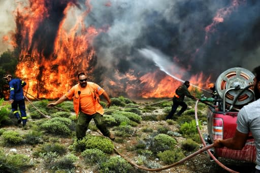 Firefighters and volunteers try to extinguish flames during a wildfire at the village of Kineta, near Athens, on July 24